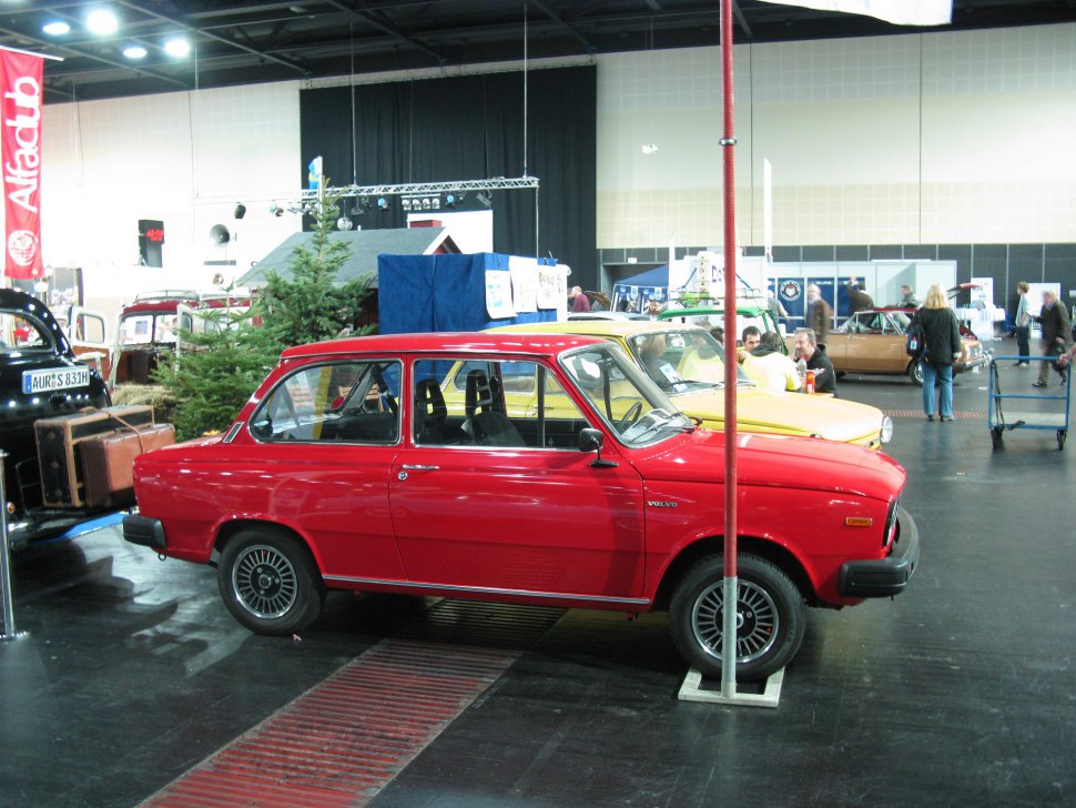 Red vintage compact sedan with black wheels, side profile.