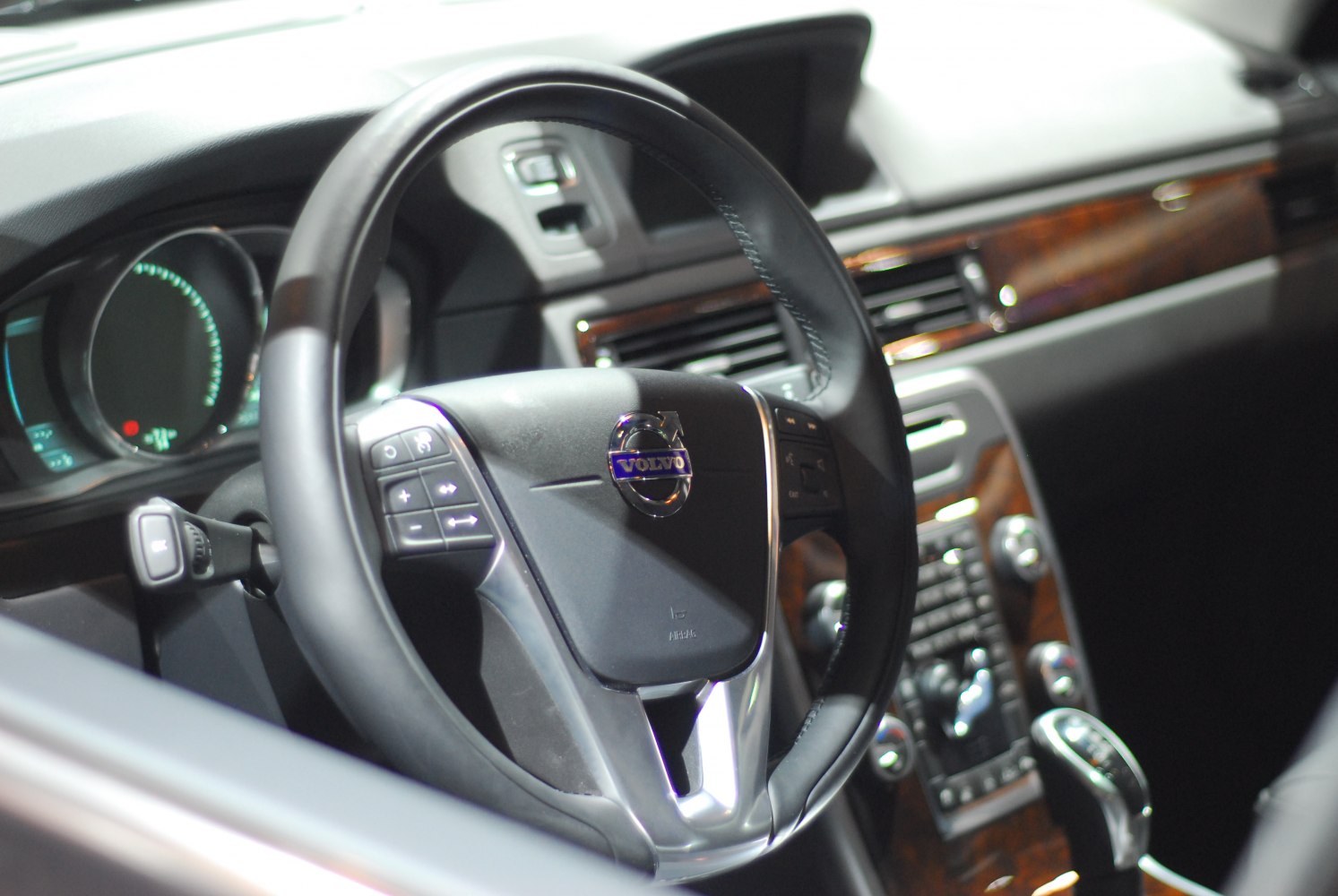 Close-up of steering wheel and dashboard with wood trim and control buttons.