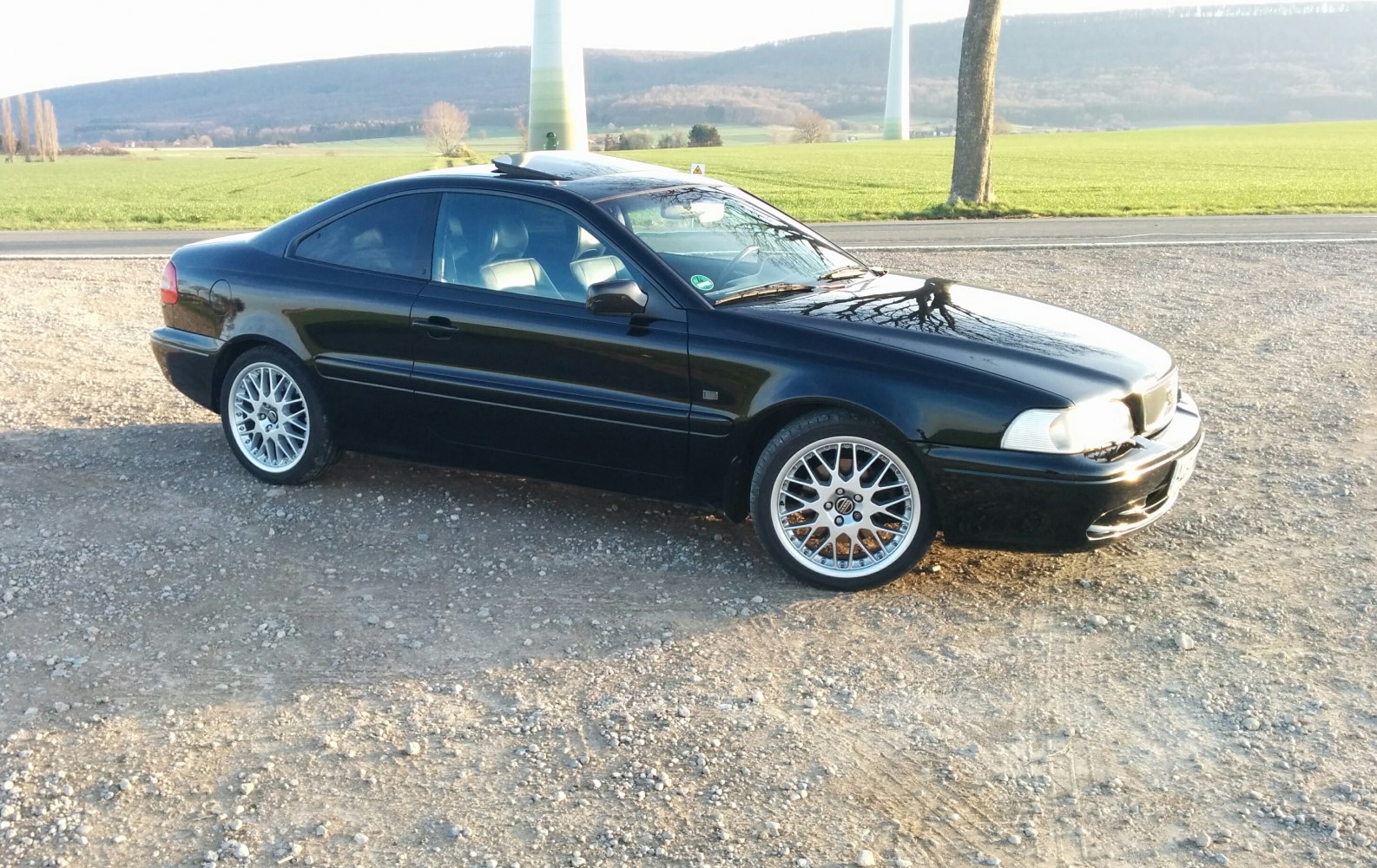Black two-door coupe with alloy wheels parked on gravel.