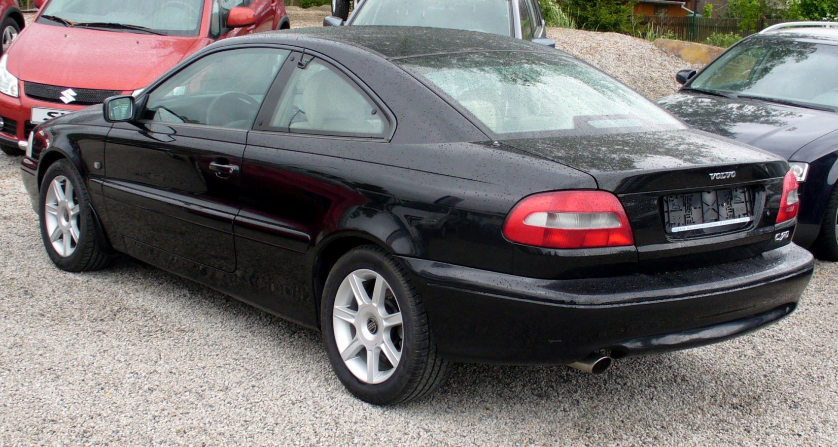 Black coupe rear and side view with alloy wheels and raindrops