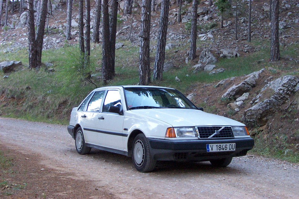 White sedan parked on a forest dirt road, front side visible.