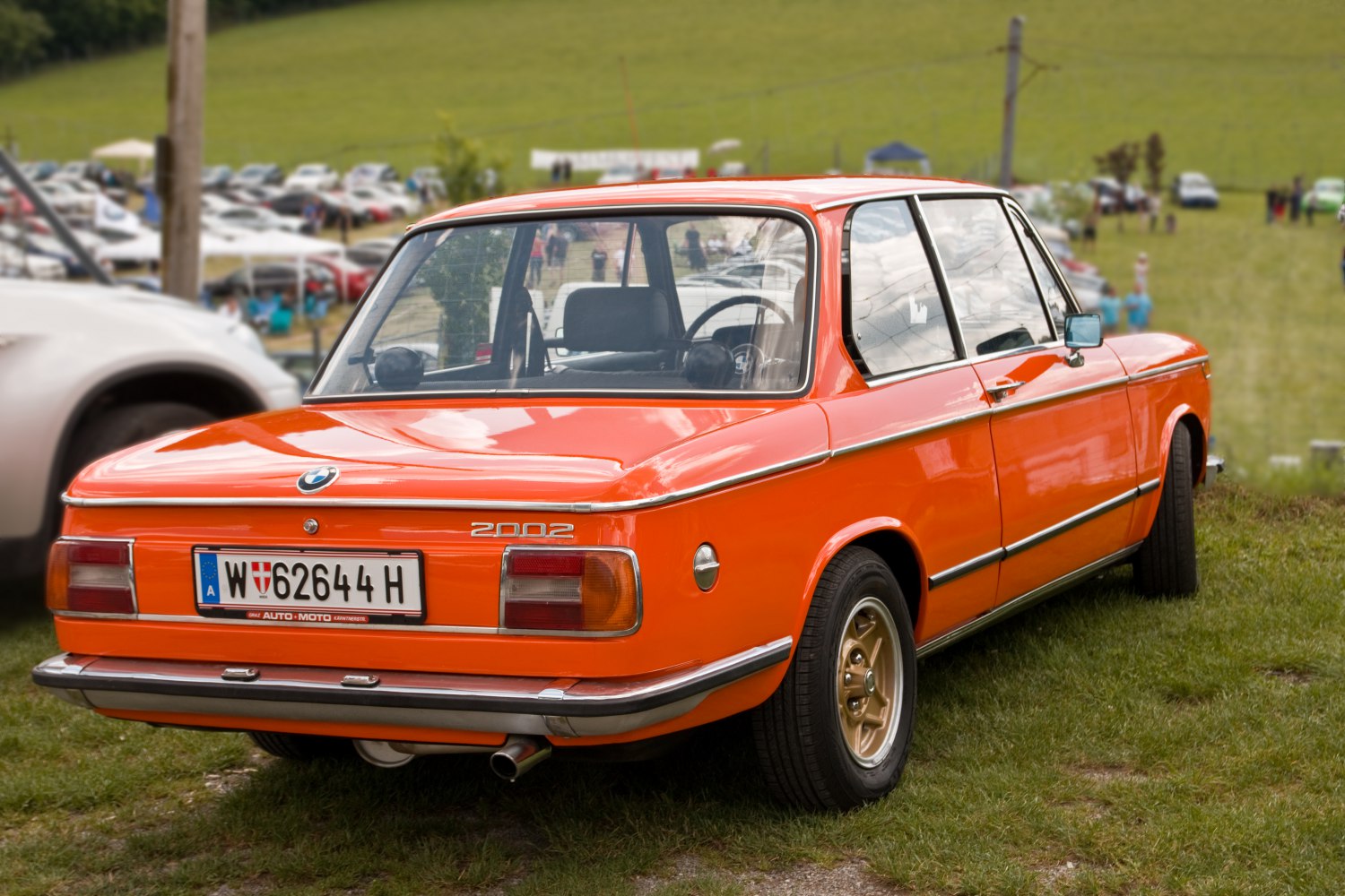 Rear view of a bright orange vintage vehicle with alloy wheels and metal trims.