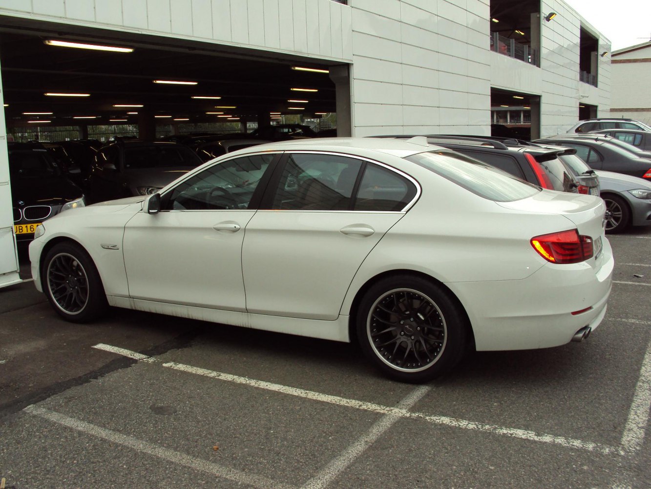 White sedan side profile with black alloy wheels and tinted windows.