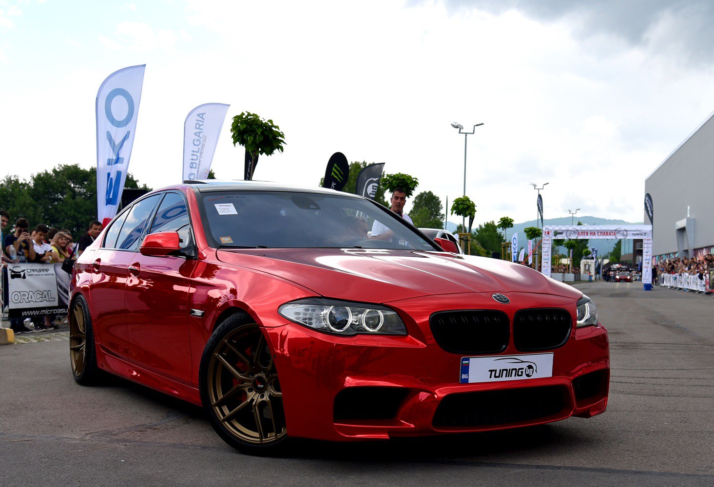 Red luxury sedan with custom bronze wheels and aggressive front bumper.