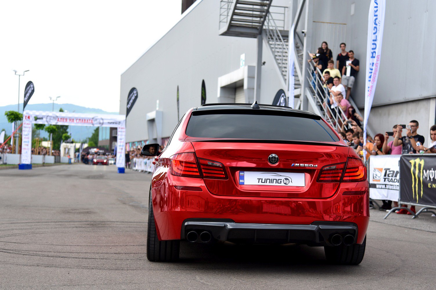 Red sports sedan rear with quad exhaust and tinted windows at event