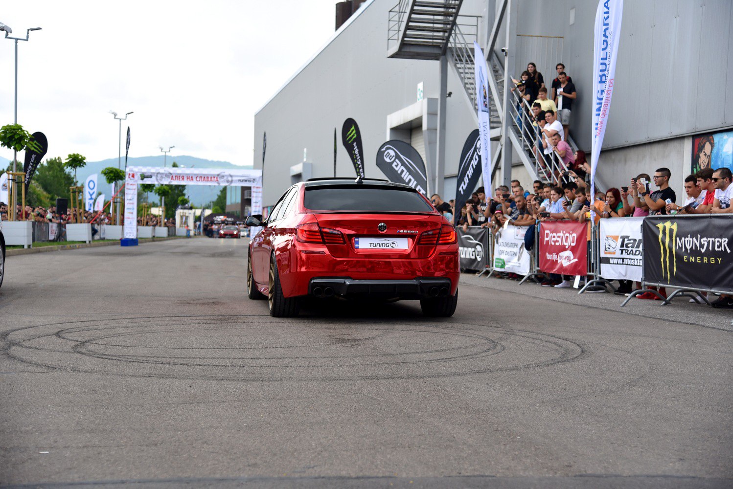 Rear view of red sedan with dual exhaust and wide tires at a packed motorsport event