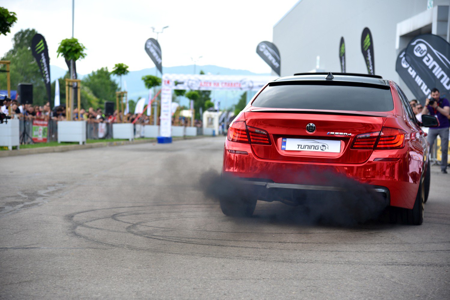 Red sports sedan performing burnout with thick black smoke.