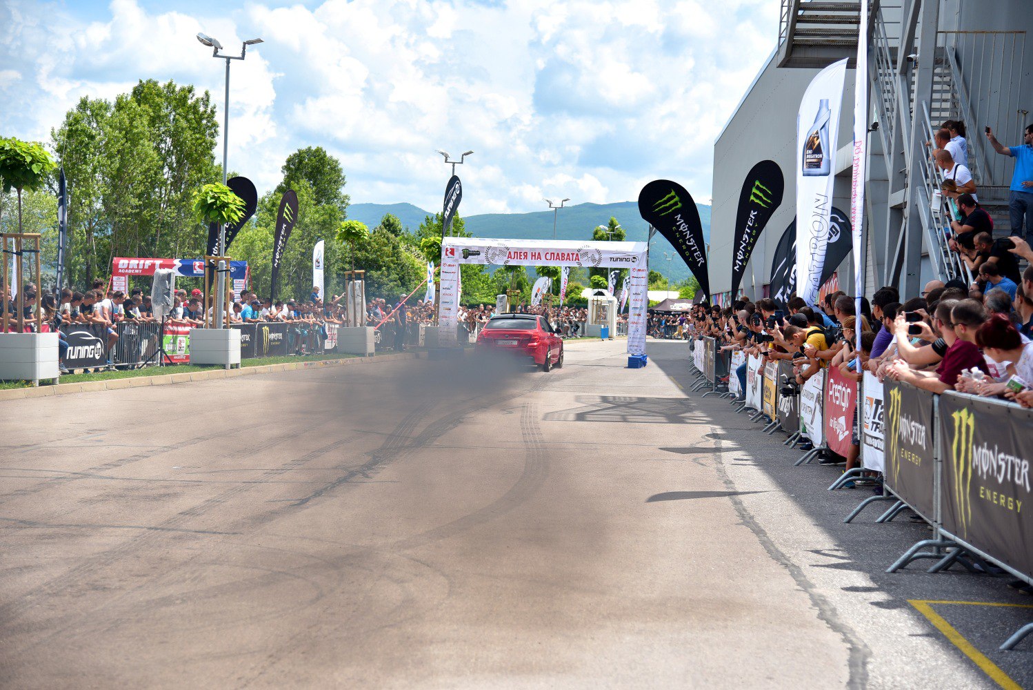 Red sedan racing with tire marks and smoke in crowded motorsport event