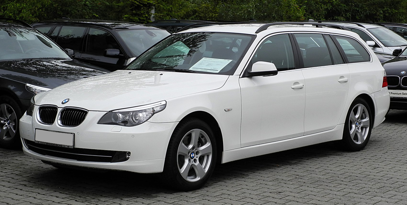 White 2007 facelift BMW 5 Series Touring with roof rails and alloy wheels.