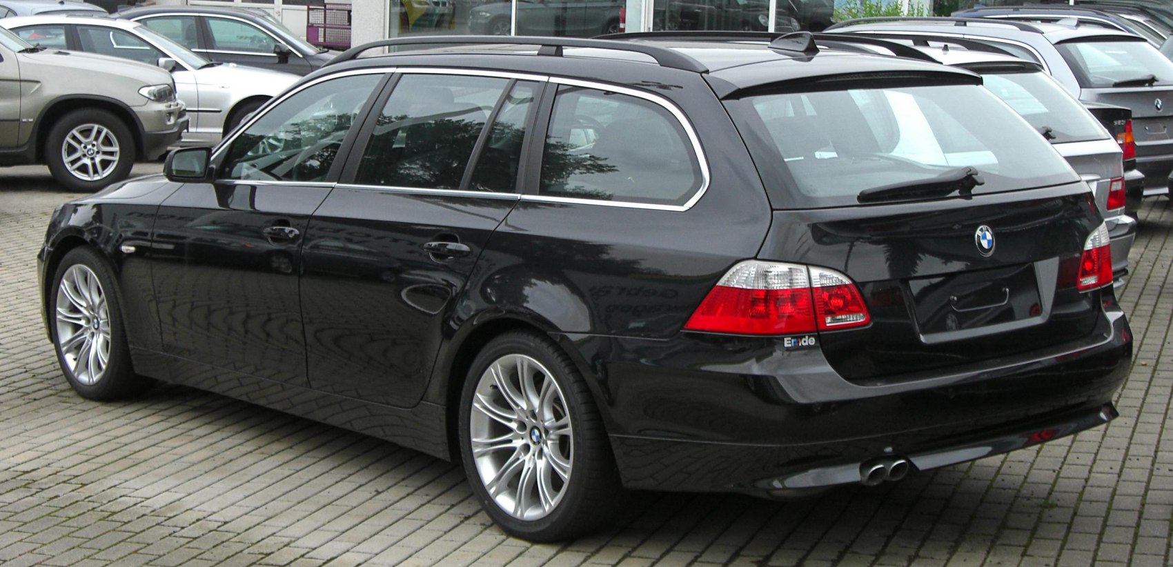 Rear side view with tail lights, alloy wheels, roof rails, and dual exhaust pipes