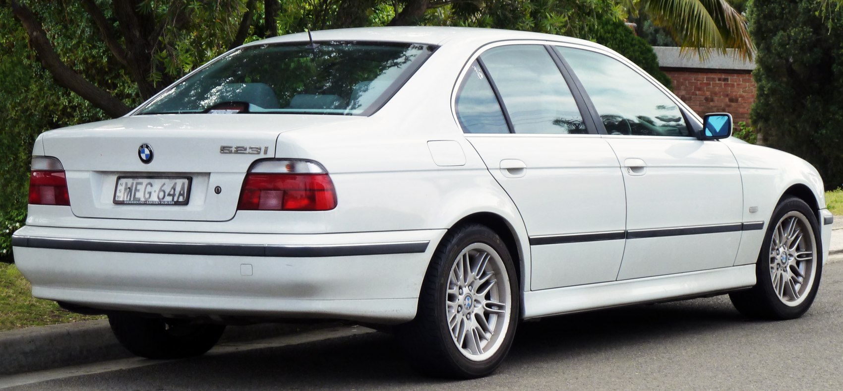 White sedan rear-side view featuring alloy wheels and classic design elements