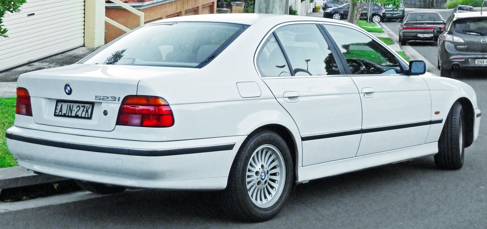 Rear side view of white four-door sedan with alloy wheels and classic rear lights.