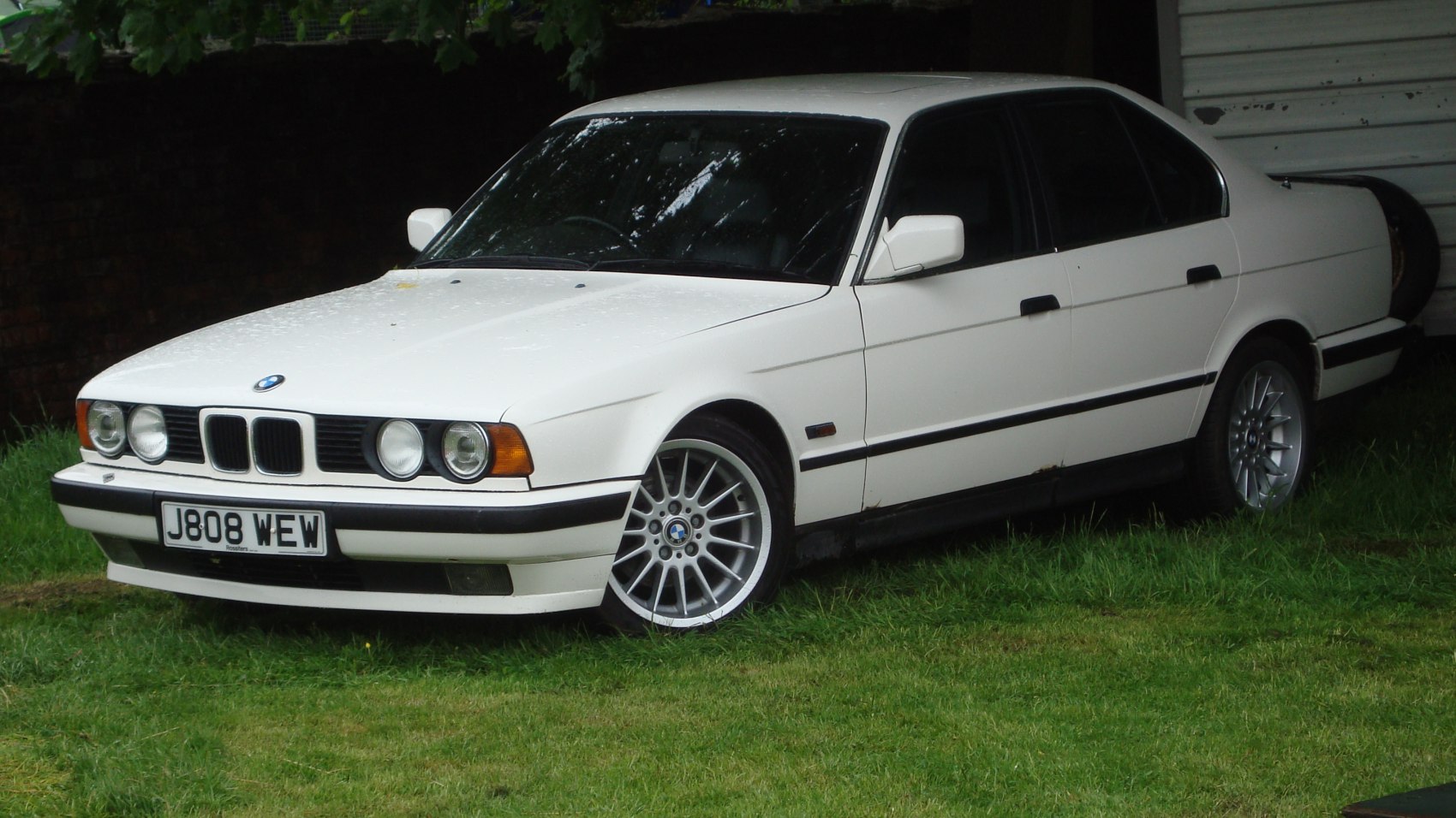 White BMW E34 5 Series sedan with quad round headlights and alloy wheels