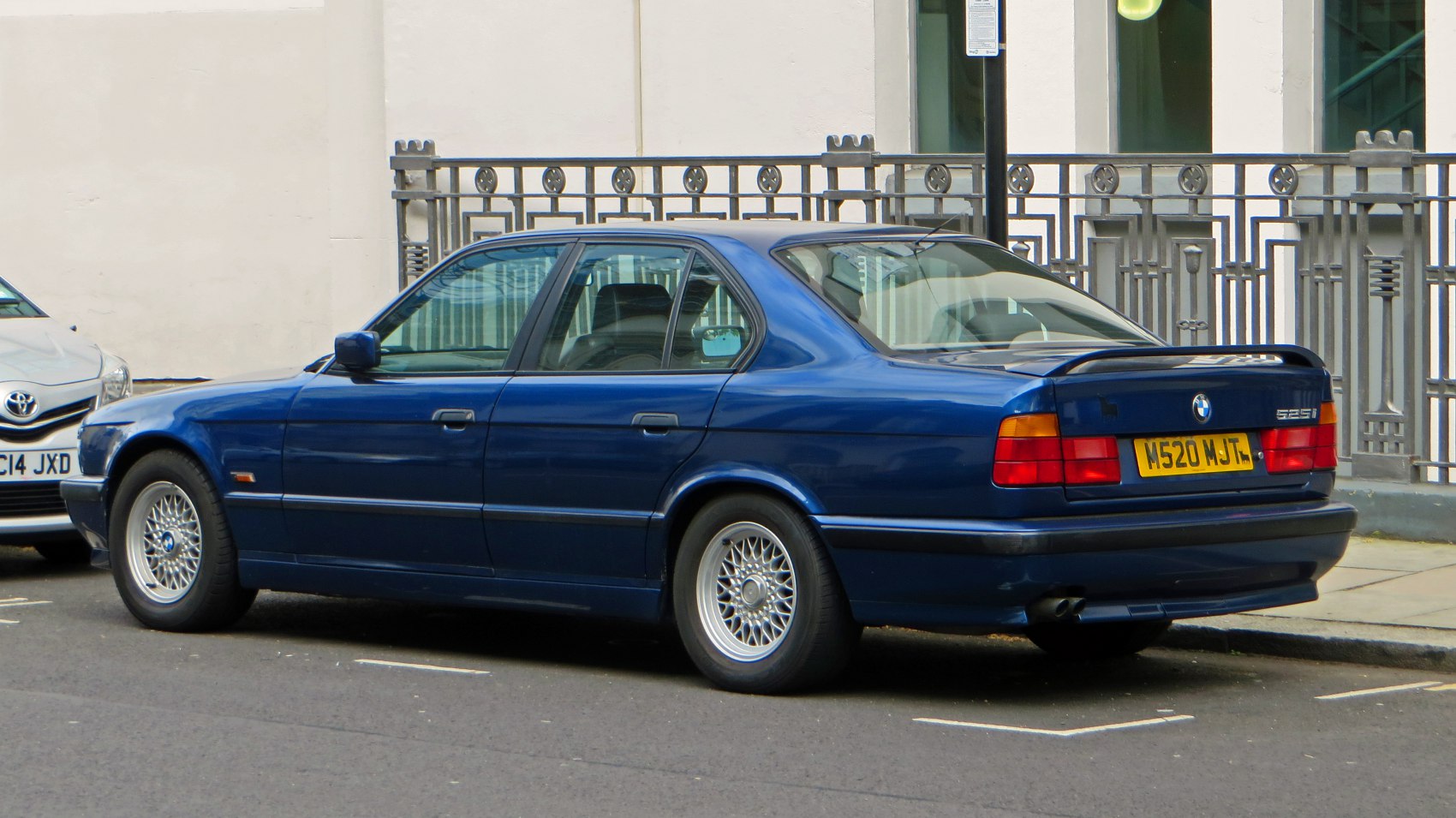 Rear side profile of a blue vintage sedan with alloy wheels and rear spoiler