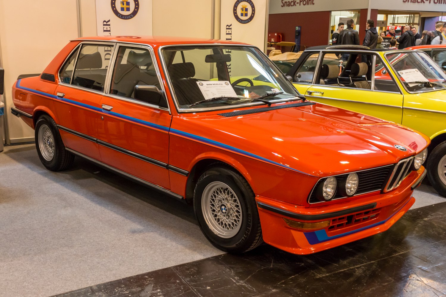 Red 1970s sedan with blue racing stripes and classic alloy wheels