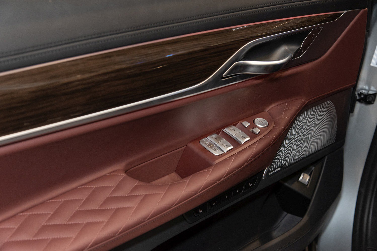 Quilted leather door panel with wood trim, chrome handle, controls, and speaker