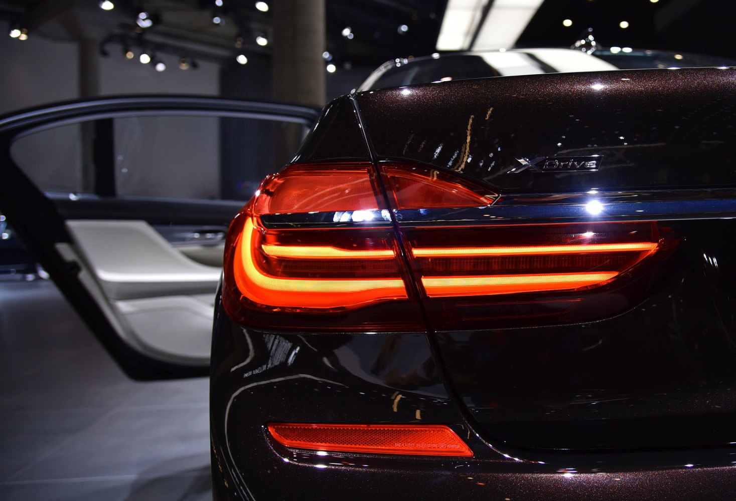 Illuminated LED tail light and open rear door in luxury sedan rear.