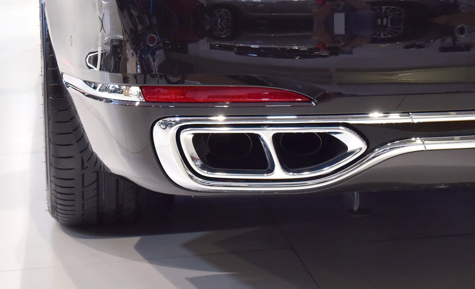 Chrome dual exhaust tips and rear light with a wide tire tread on a luxury sedan.