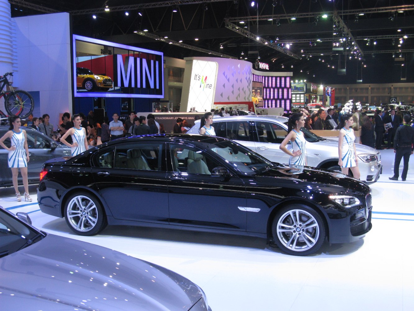 Sleek black luxury long sedan displayed with models at auto show