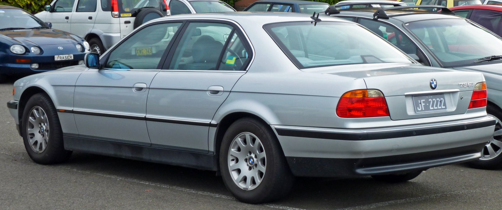 Silver luxury sedan rear-side profile with distinctive taillights and alloy wheels.