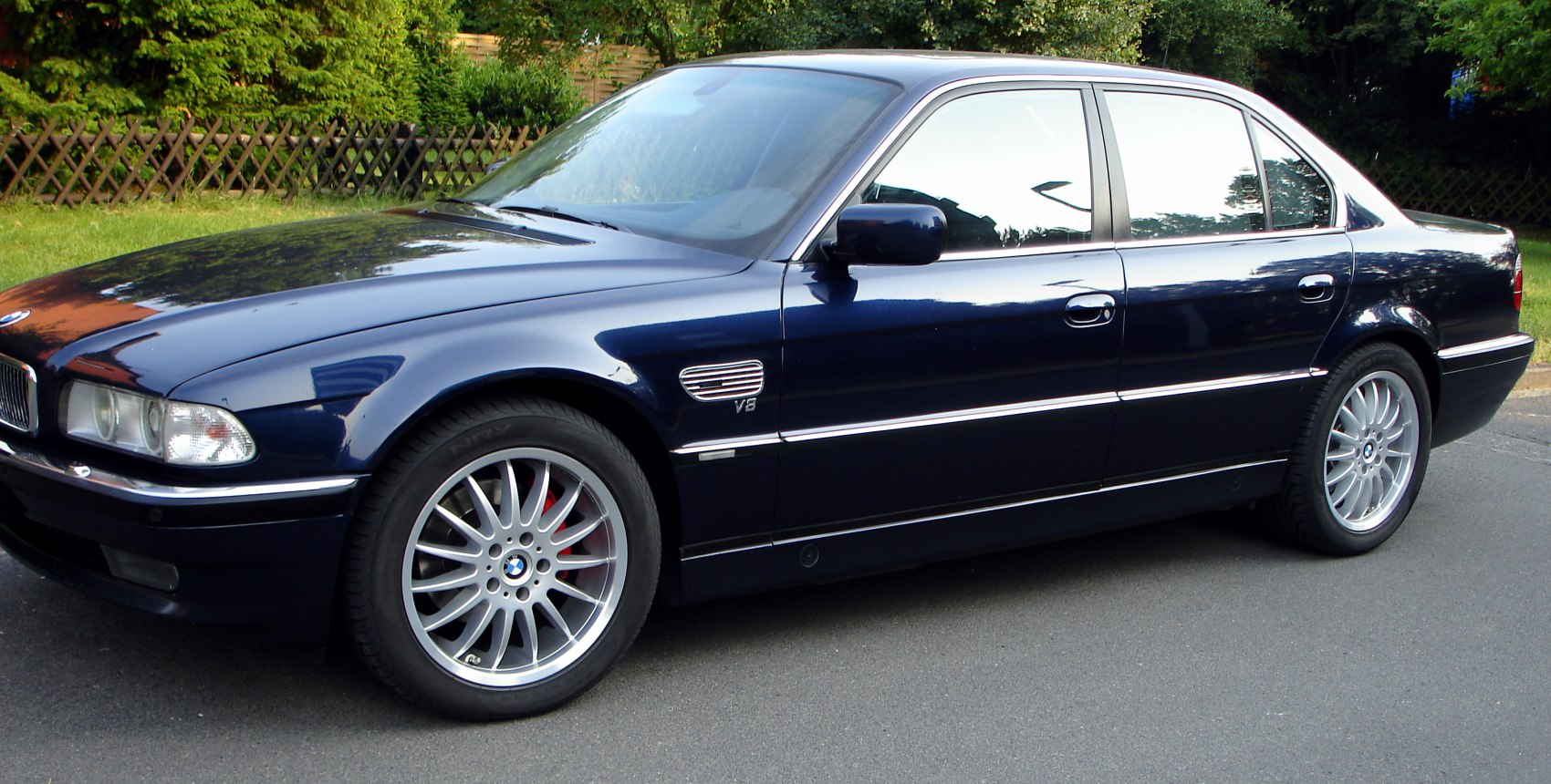 Side view of luxury sedan with V8 badge and multi-spoke alloy wheels.