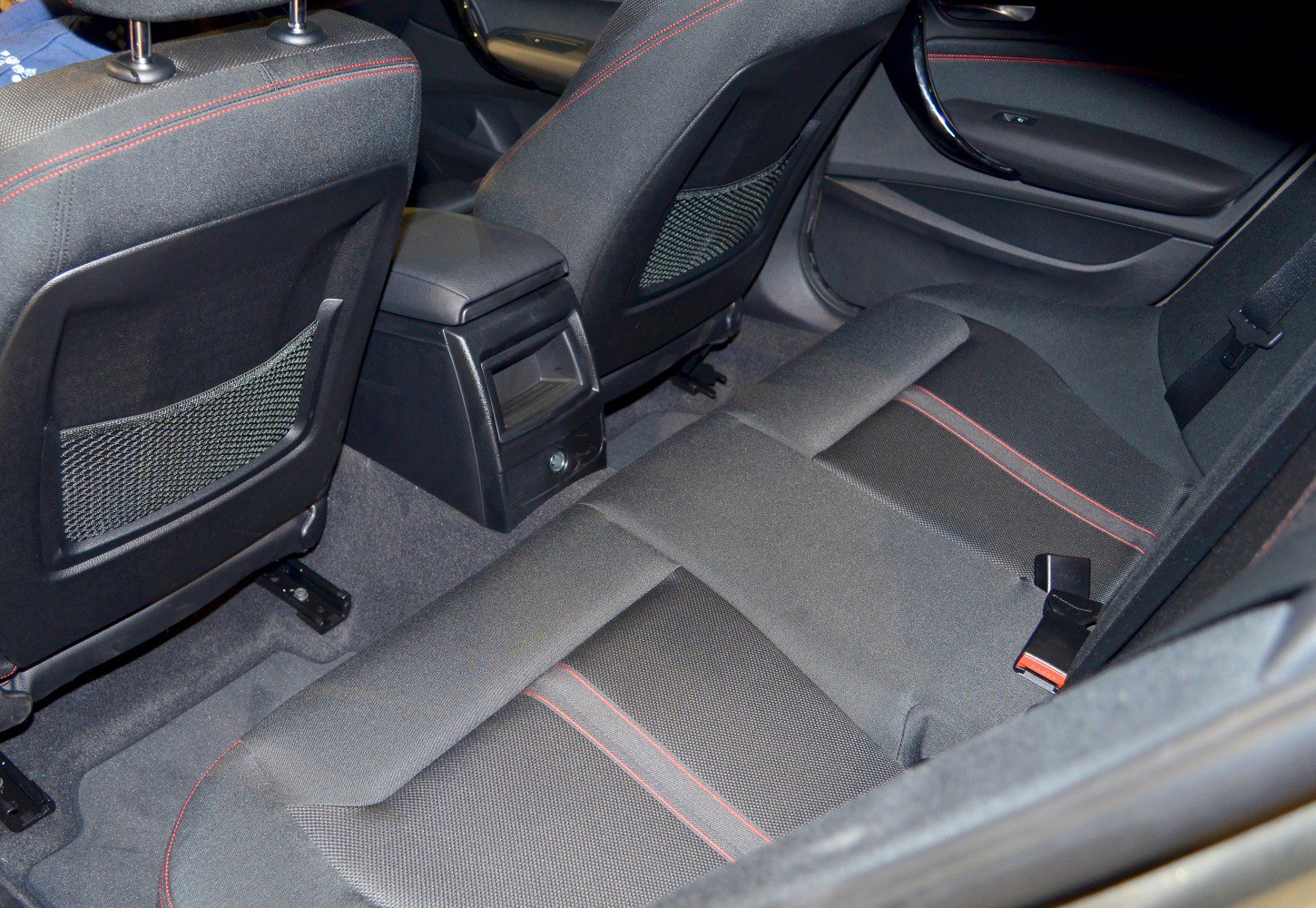 Rear seat interior with black fabric and red stitching, rear ventilation panel.