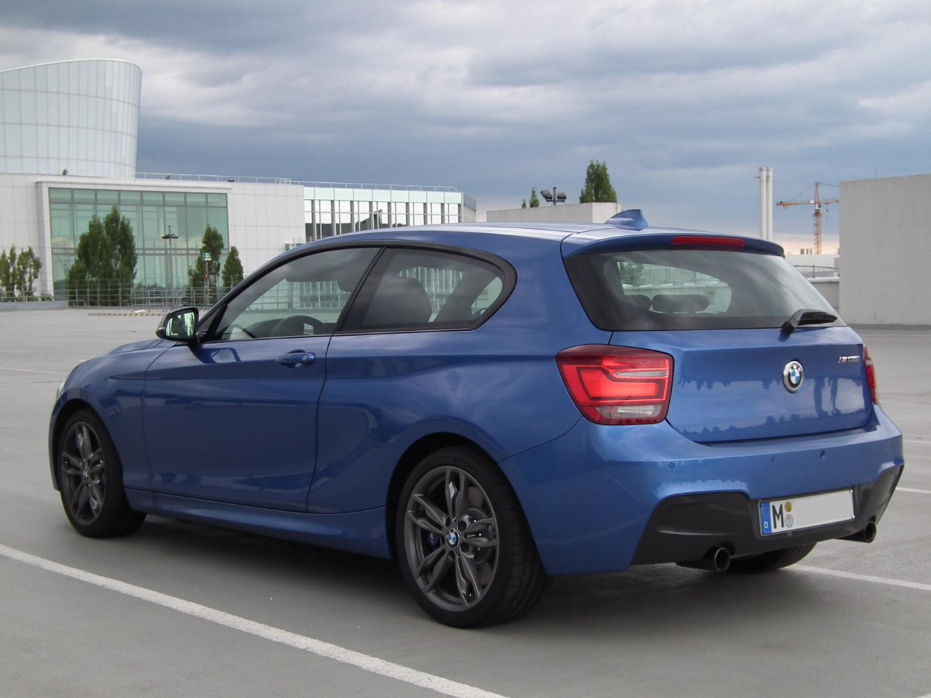 Rear-side view of blue 3-door hatchback with dual exhausts and modern tail lights.