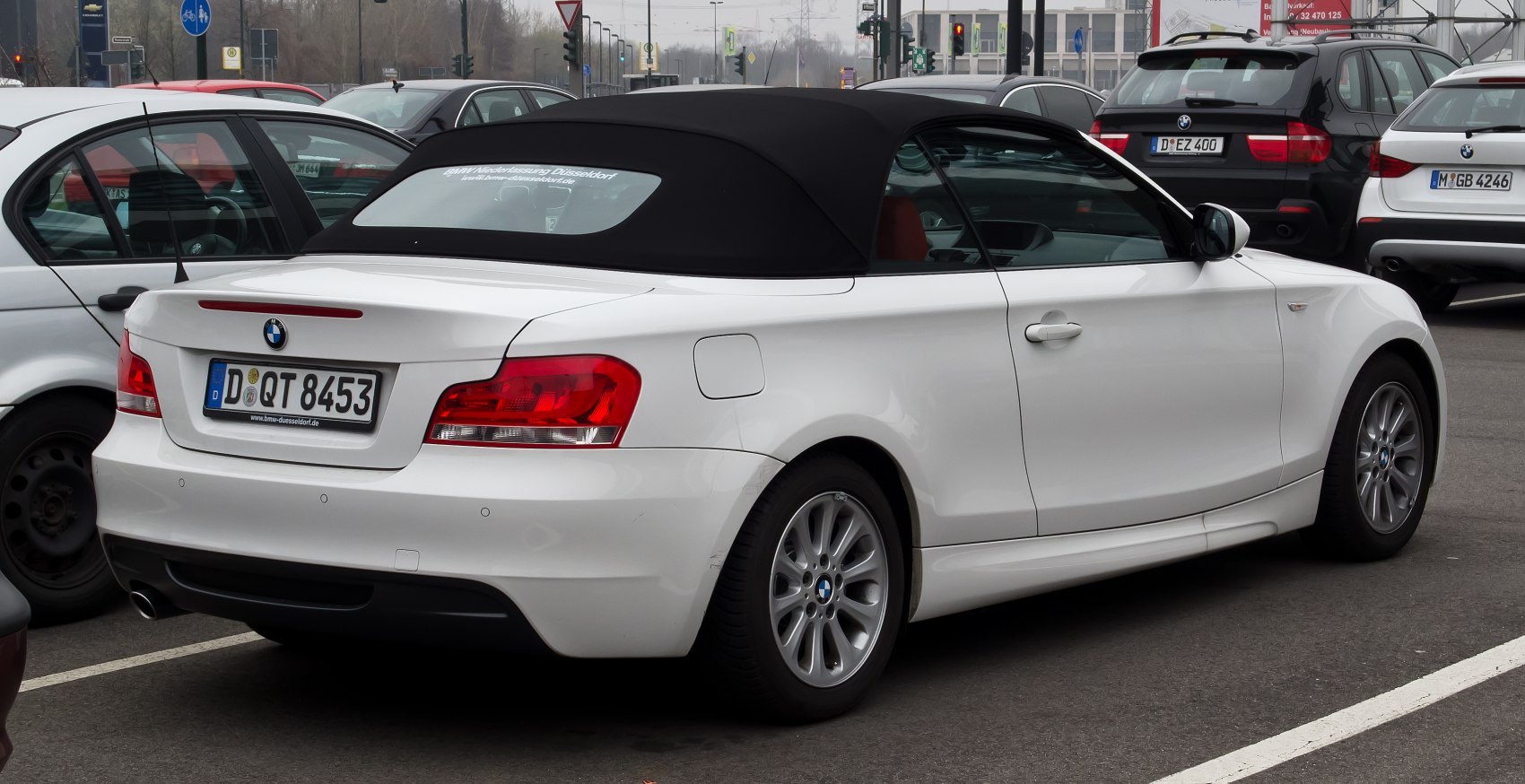 White convertible with black soft top and rear side profile in parking lot