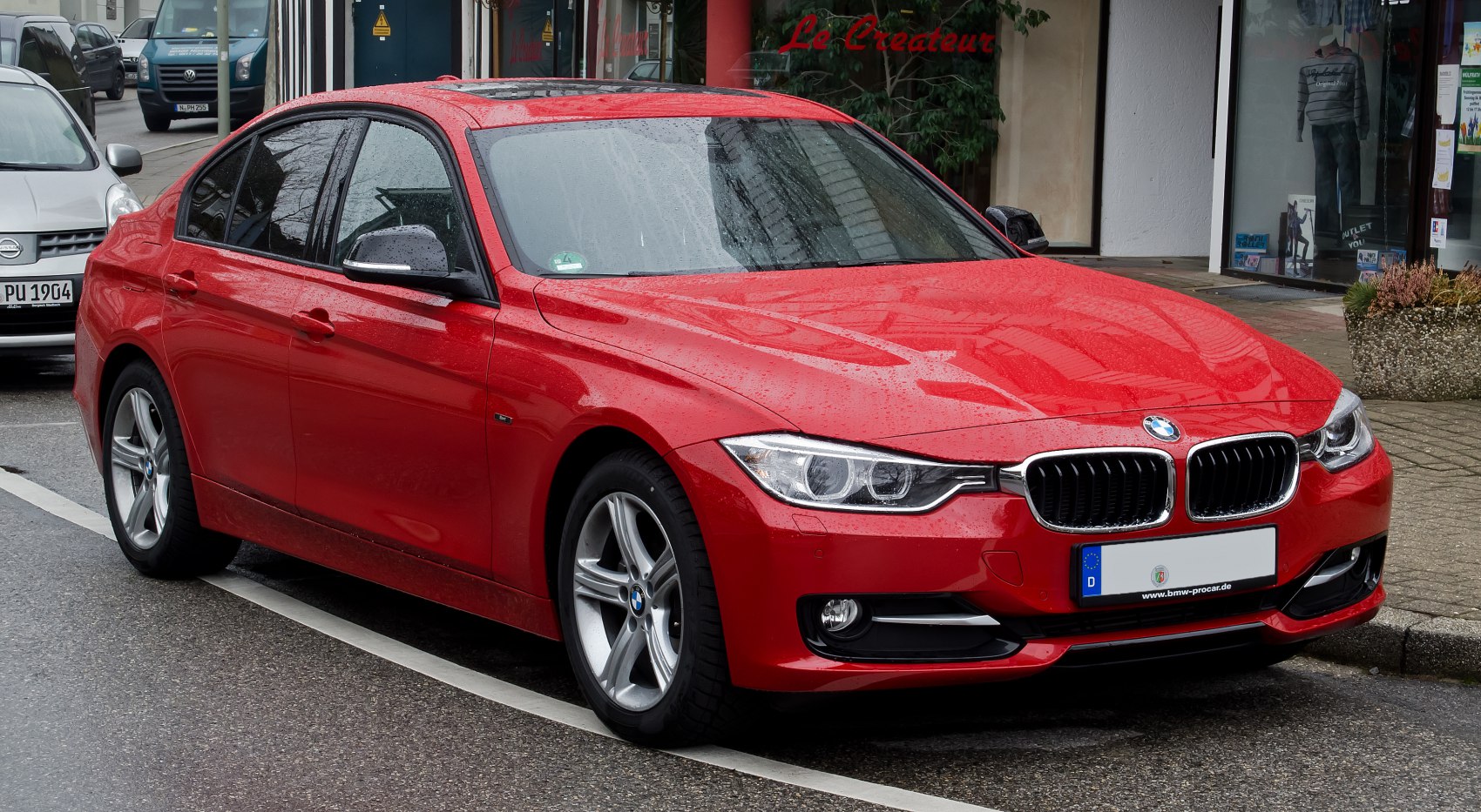 Red sedan with distinctive headlights and alloy wheels in rainy street