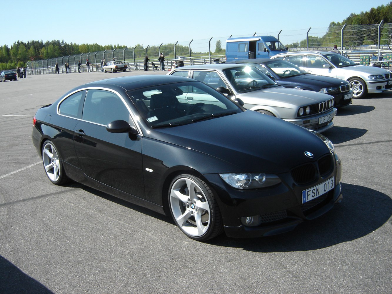 Black coupe with alloy wheels and sharp headlights in an open parking area.