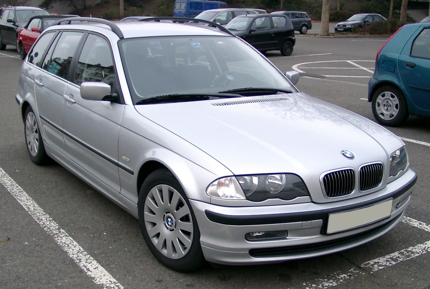 Silver station wagon with dual headlights and roof rails from front-side angle.
