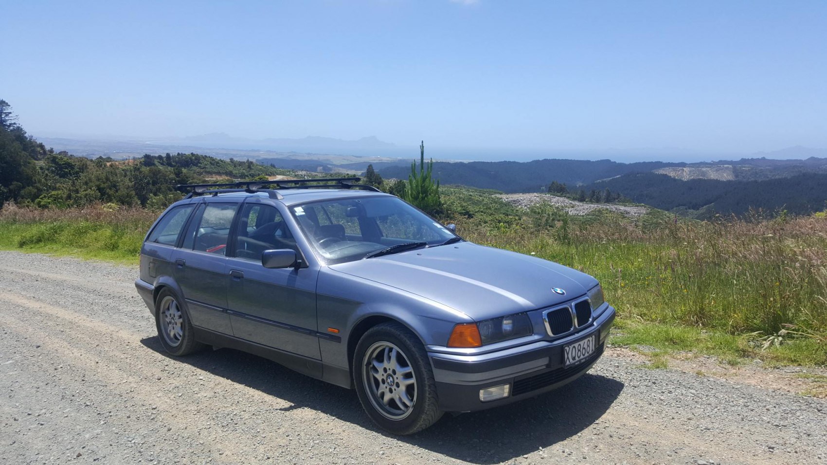 Vintage station wagon with roof rack on gravel road in scenic rural area