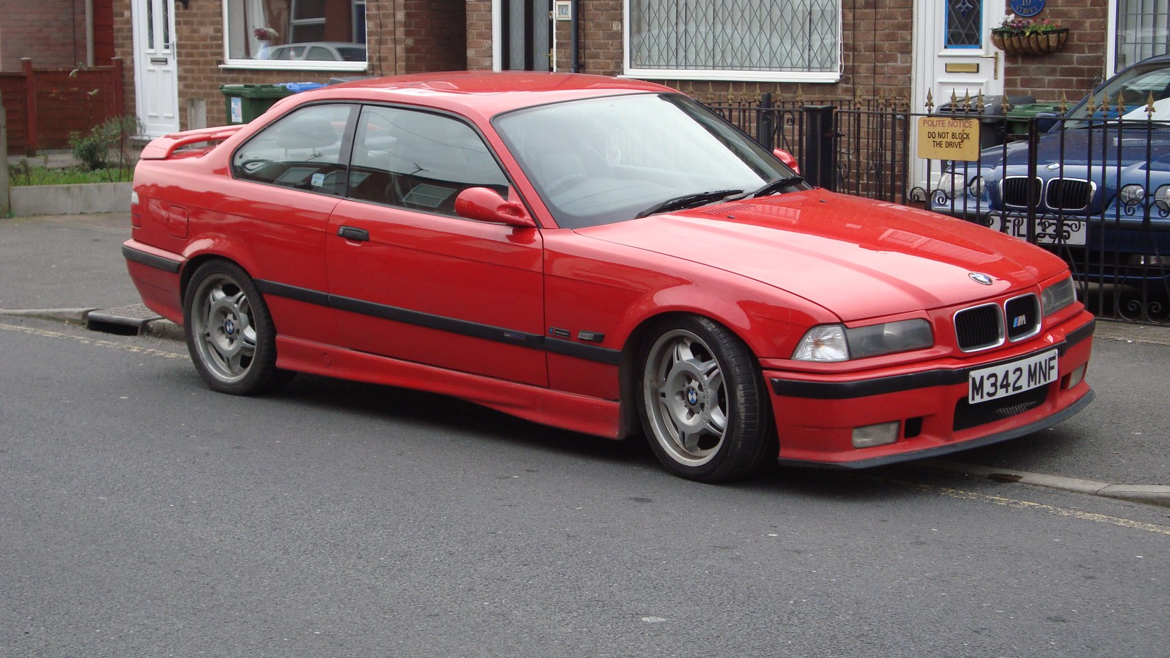 Red E36 coupe with M Sport wheels and body kit visible from front side angle