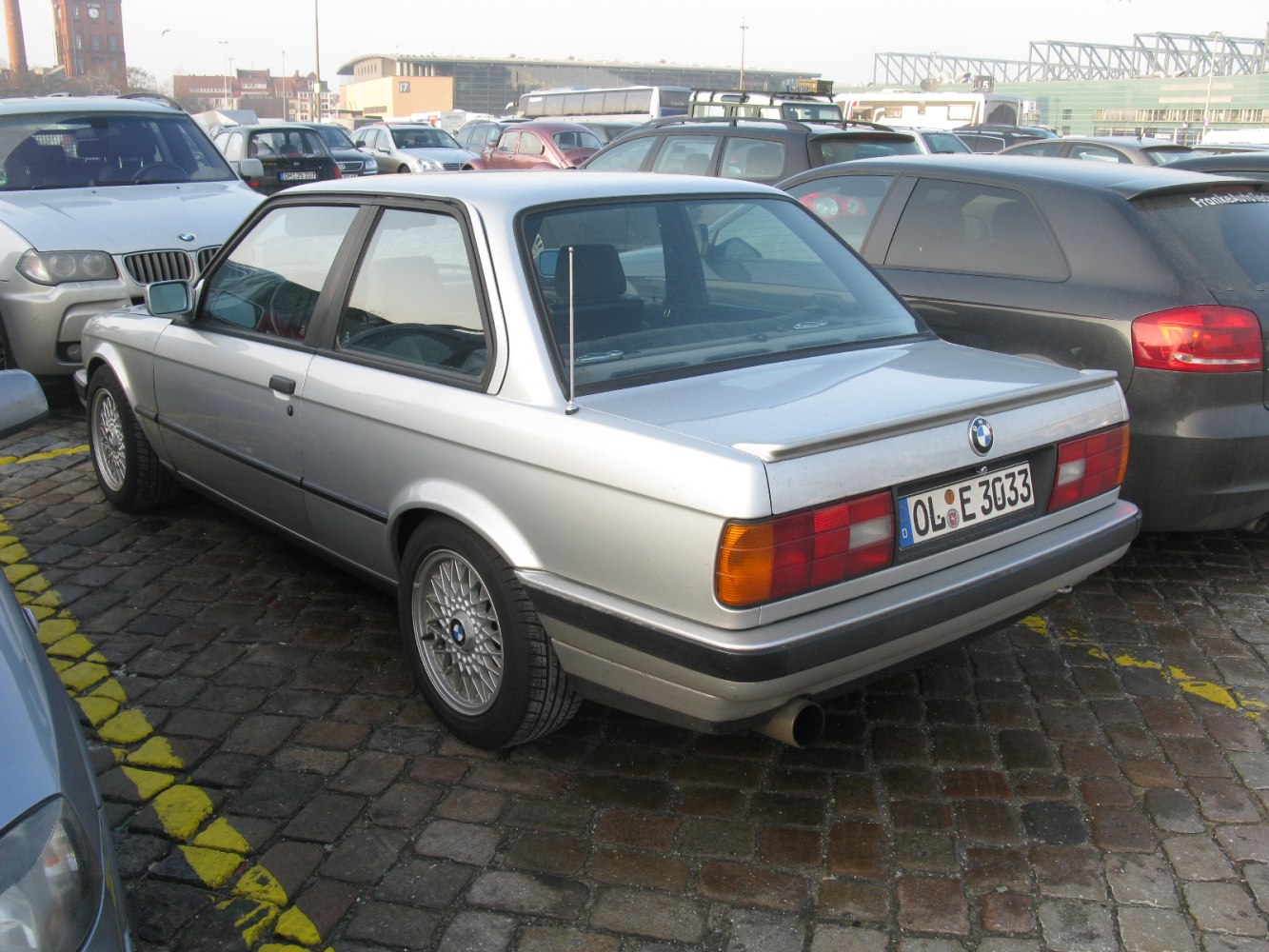 Rear-side view of silver coupe with spoiler and detailed alloy wheels