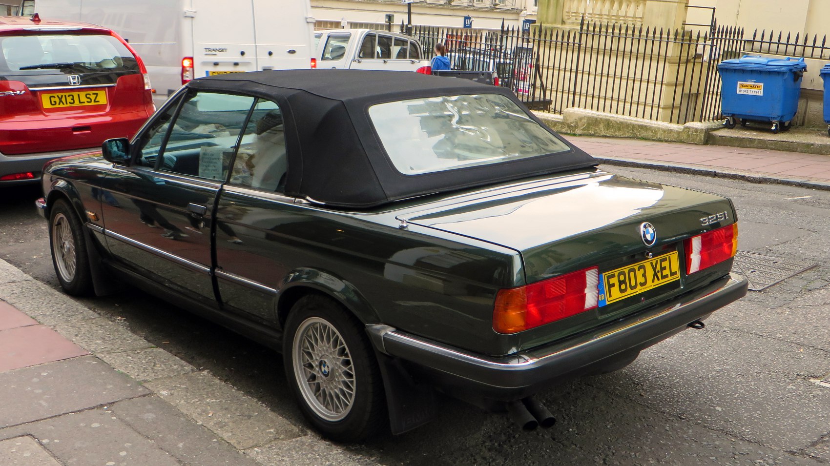 Convertible with black soft top, wire-spoke wheels, rectangular tail lights, urban parking