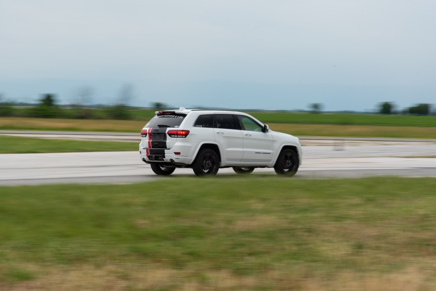 Side rear view of white SUV with tinted windows and black-red striped decal.