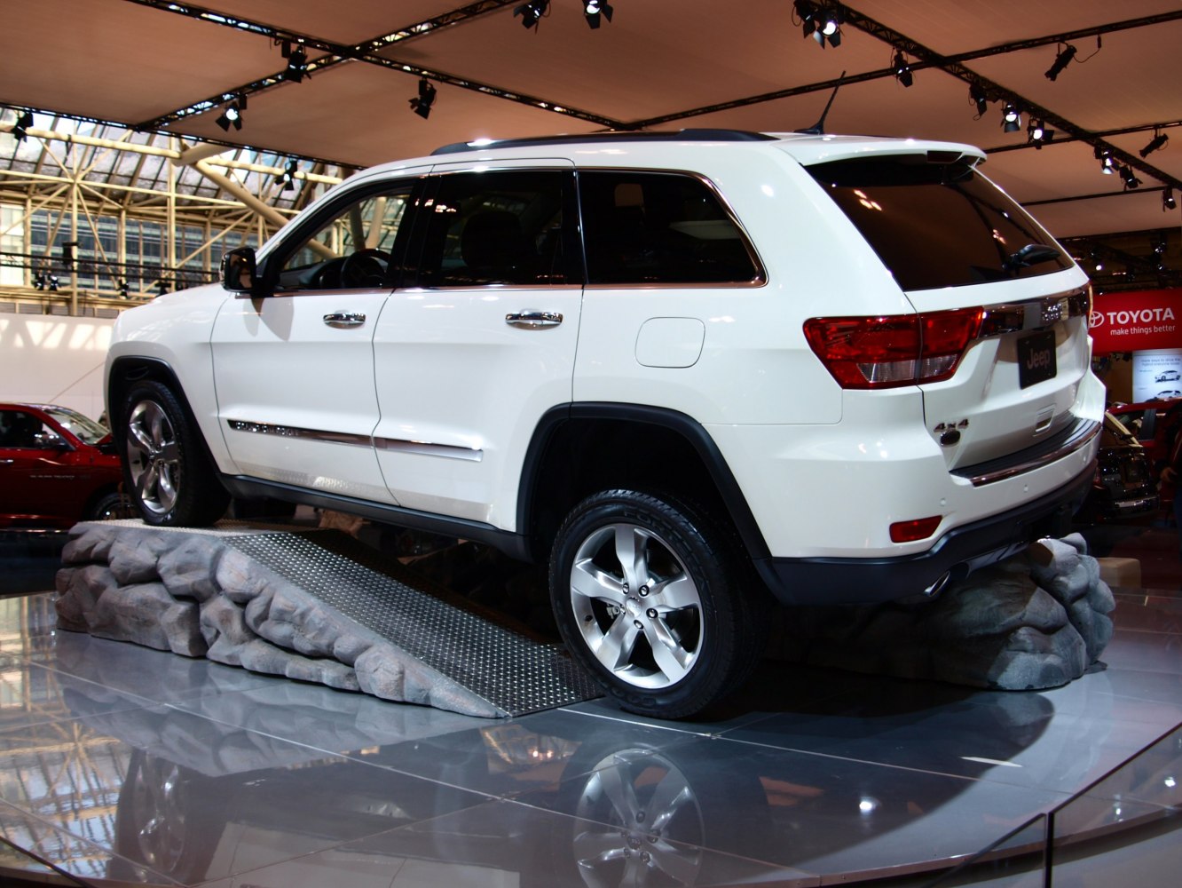 White mid-size SUV positioned on rocky inclined platform under show lighting