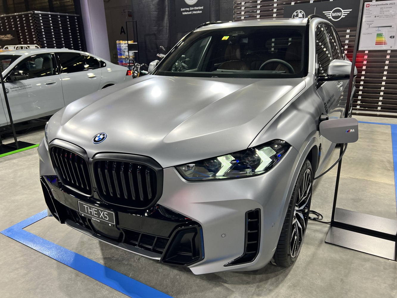 Matte silver SUV front with kidney grille and M EV charging plug.