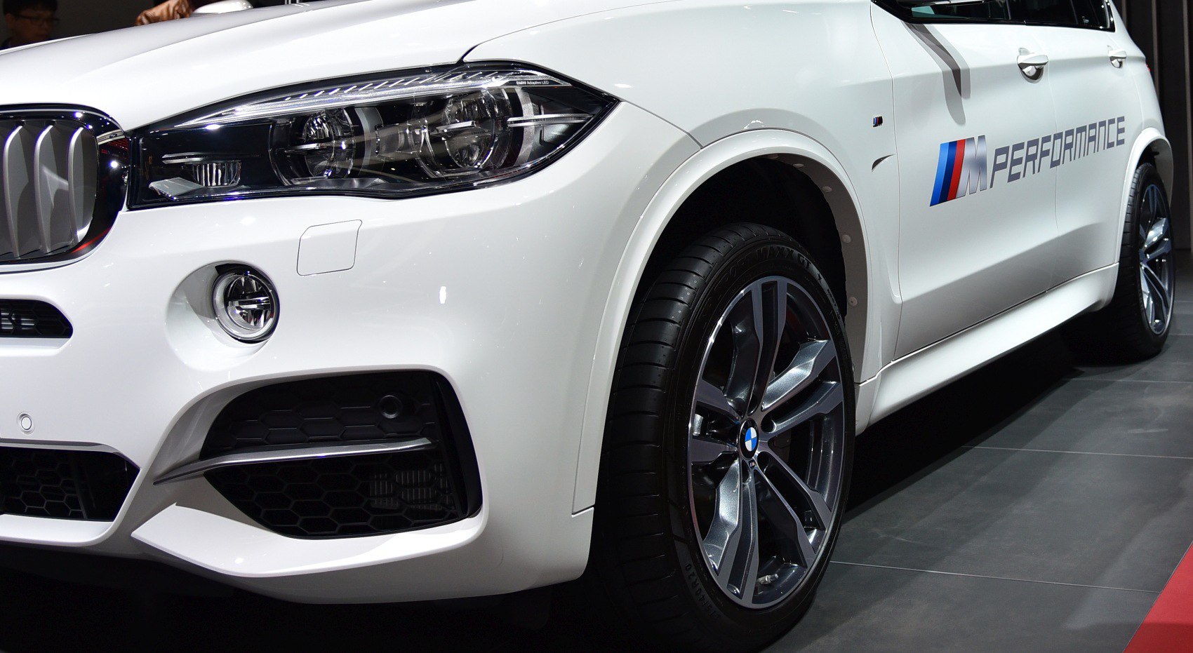 Front left headlight, alloy wheel, and M Performance side decal on white SUV