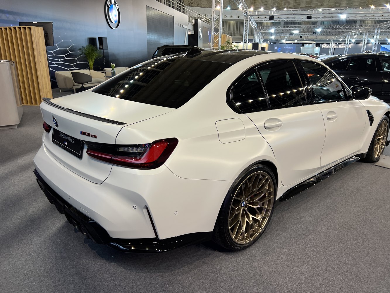 White BMW sedan rear and side with gold alloy wheels and black trim