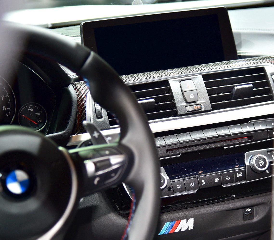 BMW interior with carbon fiber dashboard, M logo, and multi-function steering wheel