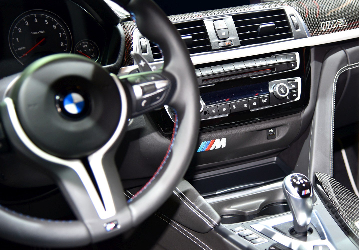 Close-up of steering wheel, dashboard controls, and manual gearshift with carbon fiber trim.