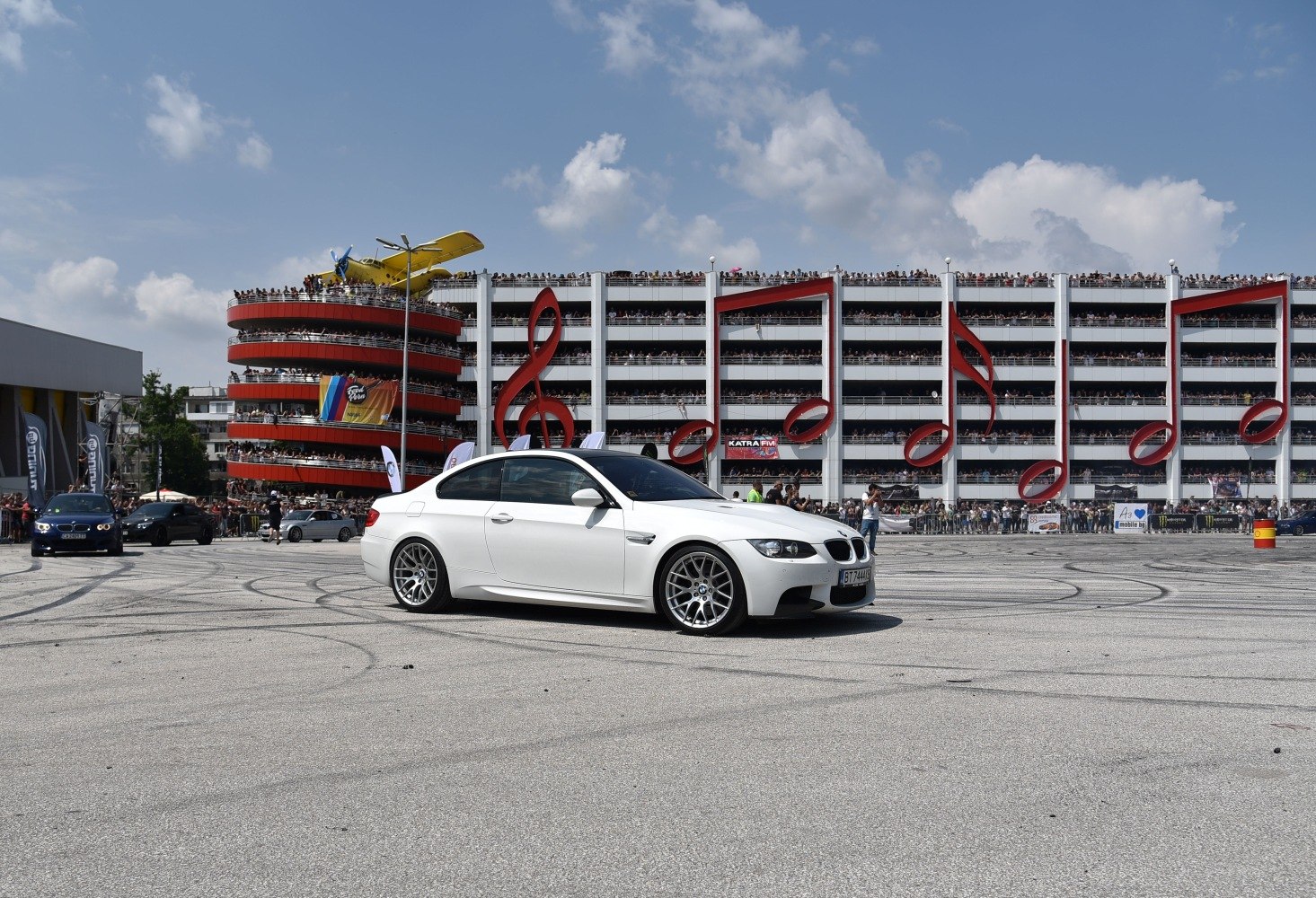 Side view of white coupe with crowd and music note structures