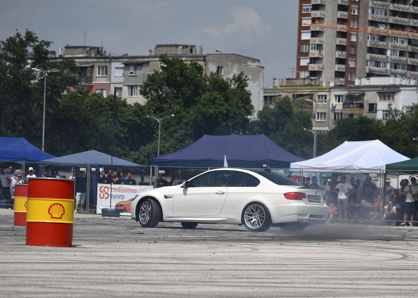 White coupe drifting with visible tire smoke on asphalt during car event.