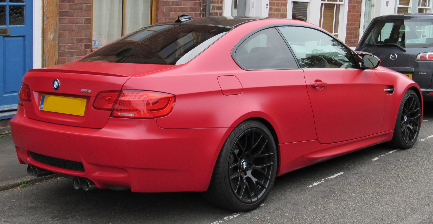 Matte red coupe rear side with black wheels and quad exhaust