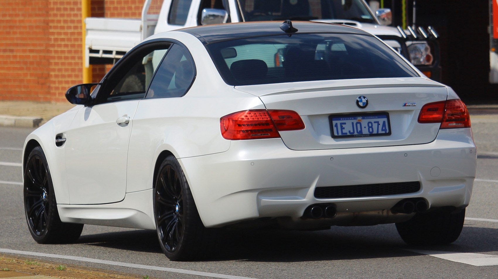 Rear view of white coupe with black rims and quad exhausts