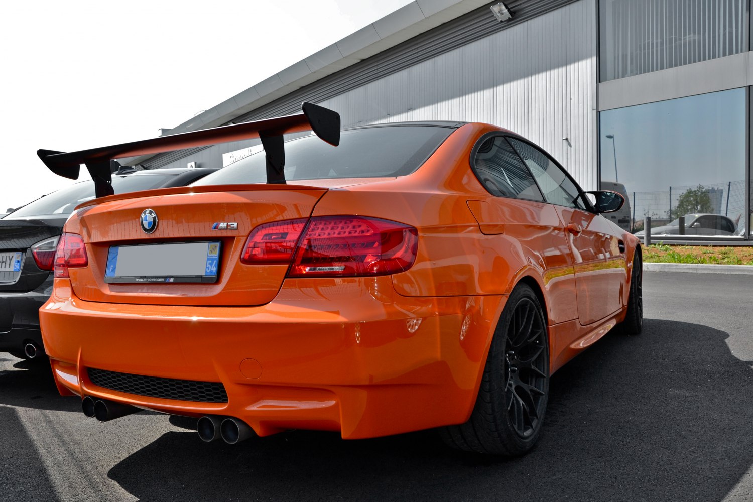 Rear view with large rear spoiler and quad exhaust tips on orange coupe