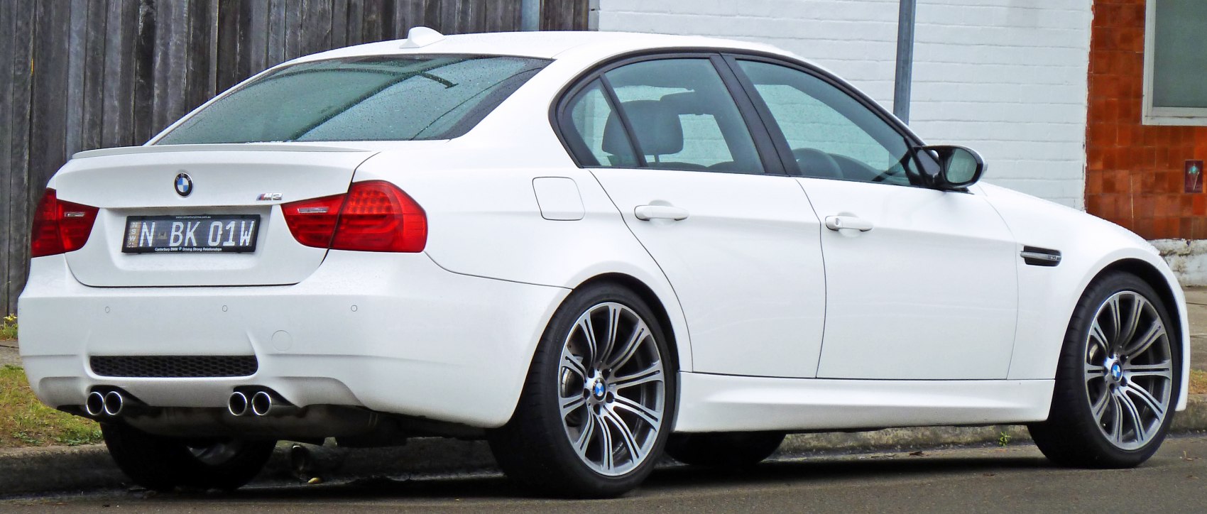 Rear side view of white sedan with quad exhaust and alloy wheels