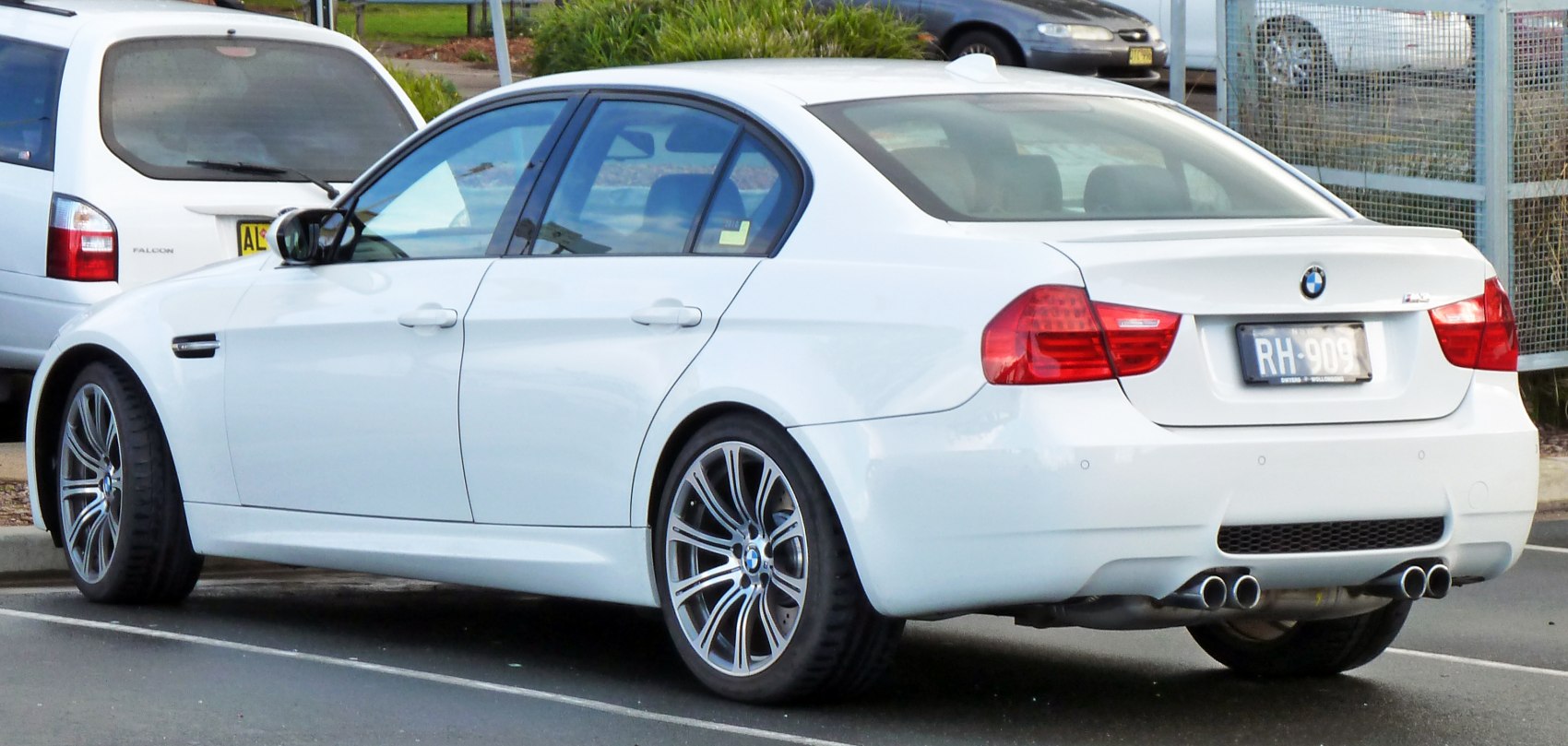 White sedan rear side view with quad exhaust and alloy wheels
