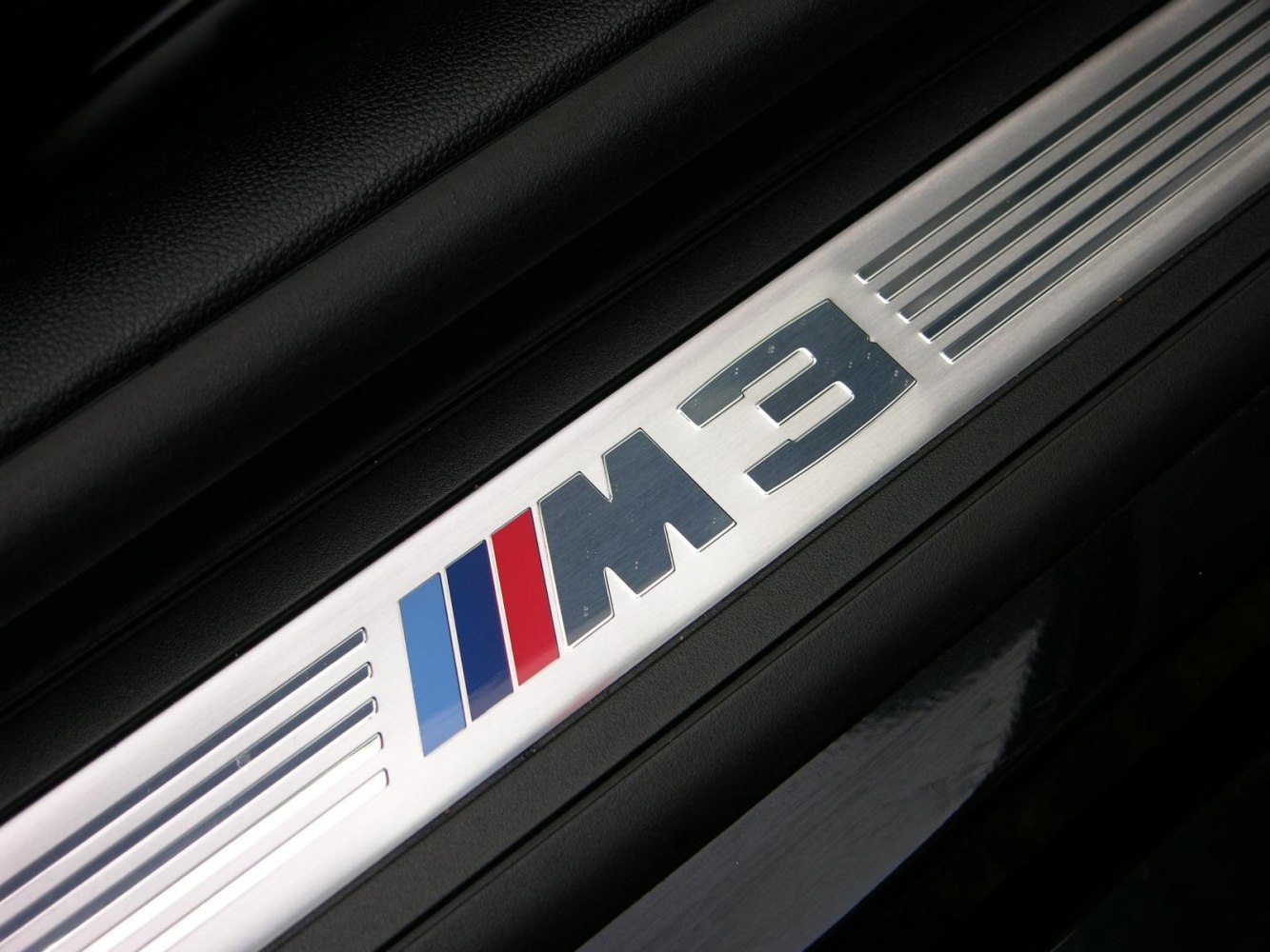 Close-up of BMW M3 E93 interior door sill plate with M3 badge and tri-color stripes